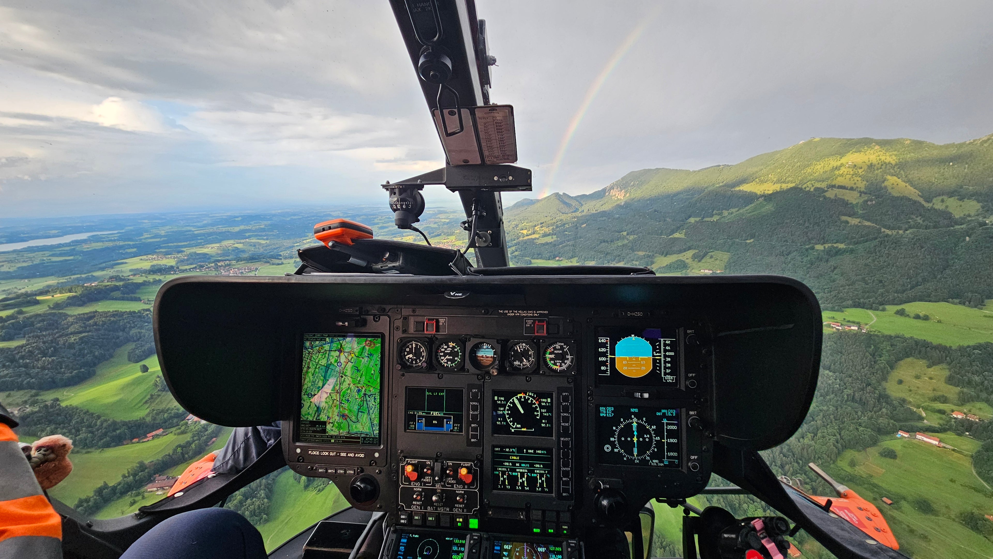 Blick aus Cockpit über grüner Berglandschaft mit Regenbgen